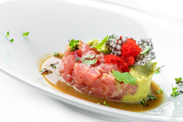 Tartar with tuna, avocado and red caviar decorated with microgreens on plate isolated on white background. Fish and seafood, close up, top view