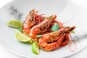 Roasted shrimps with tomatoes and lime decorated with microgreens on plate isolated on white background. Fish and seafood, close up, top view