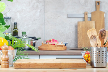 Kitchen table with cutting board, spice grinder, vegetables and utensils, countertop with pans on...