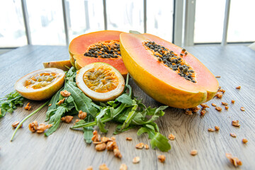 Slices of sweet papaya, maracuja, green rucola surrounded by granola flakes on a wooden background