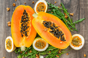 Slices of sweet papaya, passion fruit and rucola surrounded by granola flakes on a wooden background