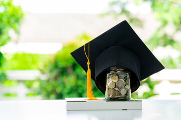 A graduation cap placed over a jar of coins on top of a book.