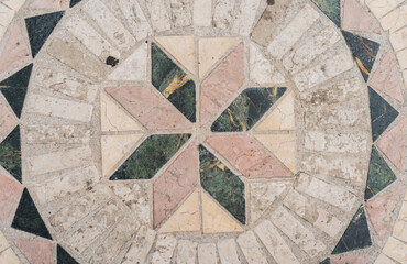 Mosaico decorativo de piedra con diseño floral geométrico sobre superficie de concreto