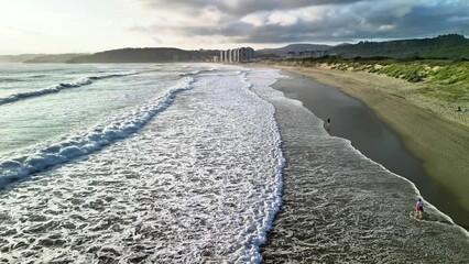 A serene beach at sunset has gentle waves lapping at the shore and beautiful coastal views