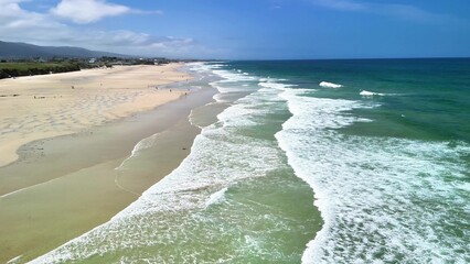 A beautiful coastal beach that features gentle waves lapping at the shore under clear blue skies