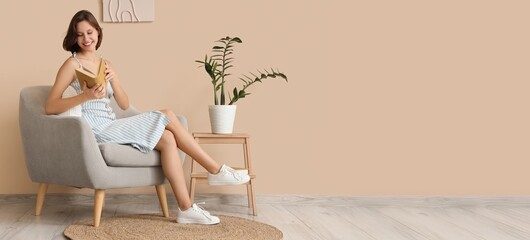 Pretty young woman reading book while sitting in armchair. Banner for design