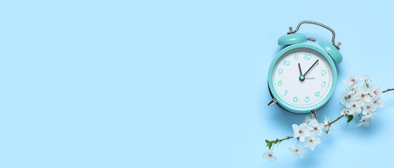 Alarm clock and blooming branch on blue background. Spring time