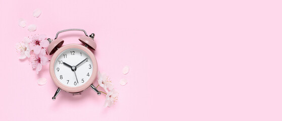 Alarm clock and flowers on pink background. Spring time