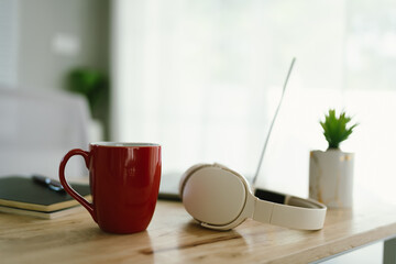 A modern, minimalist desk workspace with a laptop, headphones, notepad, cup of coffee, and houseplant, ready for productive remote work.