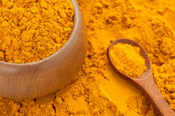 Finely dried turmeric powder in a bowl and wooden spoon - Curcuma longa