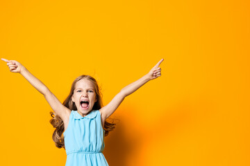 Joyful little girl in a blue dress with arms raised, celebrating against a vibrant orange background