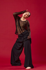 Fashion, asian woman in black pants and sheer top posing on red background with hands on hips and head tilted to the side