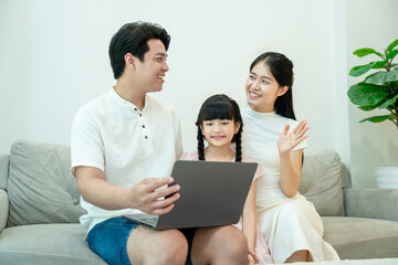 Happy Asian family making a video call on a laptop. The mother waves at the screen to greet family or friends online.