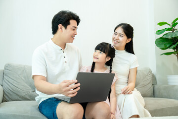 Fototapeta premium An intimate family moment of connection. Parents and daughter smile and look at each other while spending quality time with a laptop.