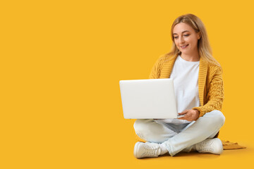 Naklejka premium Mature woman using laptop on yellow background