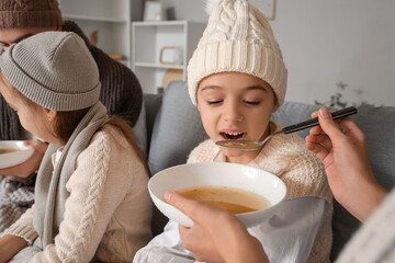 Ill little girl with her mother eating soup at home, closeup