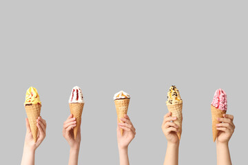 Female hands with different sweet ice-cream in waffle cones on grey background