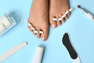 Young woman with toe separators and different tools for pedicure on blue background