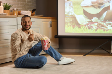 Young man with popcorn watching movie on projector screen in kitchen at night