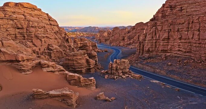 Aerial shot of a winding asphalt road through dramatic yardang landform rock formations at sunset in Xinjiang, China.