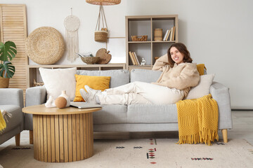 Plakat Pretty young woman lying on grey sofa in light living room