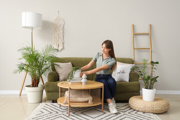 Young woman sitting on green sofa with plant in living room