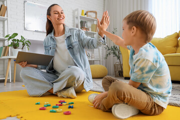 Female speech therapist with little boy giving each other high-five in office