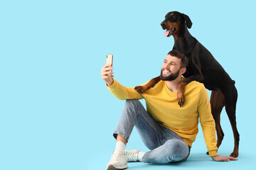 Young man with Dobermann dog taking selfie on blue background