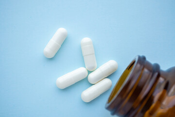 medicine pills capsule spilling out of bottle on blue background