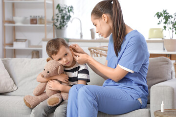 Female doctor examining little boy's ear with hearing problem at home