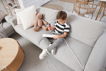Cute little boy playing with screwdriver and extension cord on sofa at home. Child in danger