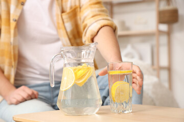 Young man taking glass of lemon infused water from table at home, closeup