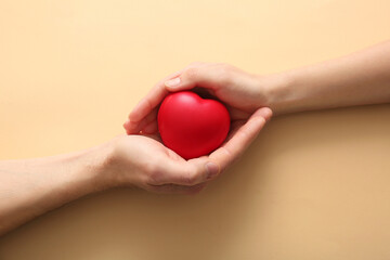 Couple holding heart on beige background, top view