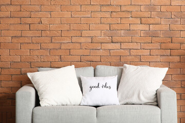 Grey sofa with white cushions near brick wall in living room