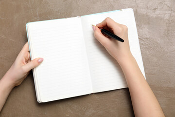 Obraz premium Female hand writing in open lined notebook with pen on textured brown background, top view for business and education