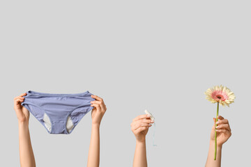 Female hands with period panties, tampon and flower on grey background