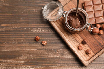 Jar of sweet chocolate spread and hazelnuts on wooden background