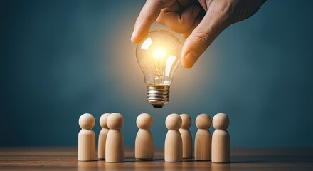 A hand holds a glowing lightbulb over a group of wooden figurines