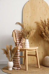Chair with plaid, screen and pampas grass in vases near white wall in room