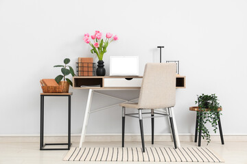 Interior of modern workplace with stools, houseplants, laptop and beautiful tulip flowers in vase