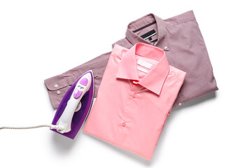 Modern electric iron with folded clean shirts on white background