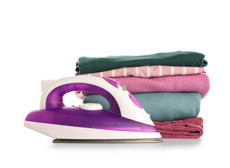 Modern electric iron with stack of folded clean clothes on white background