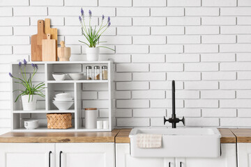 Stylish sink, beautiful Muscari flowers, kitchen utensils and spices on  counter near light brick...
