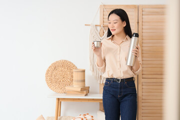 Young Asian woman with thermos at home