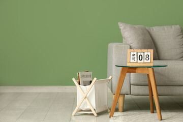 Table with flip calendar, sofa and magazine stand near green wall in living room