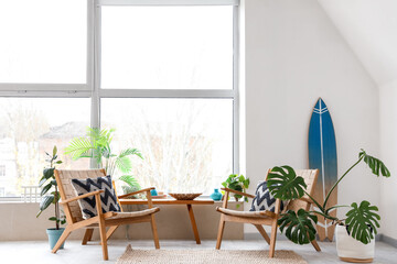 Interior of light room with surfboard, armchairs and plants