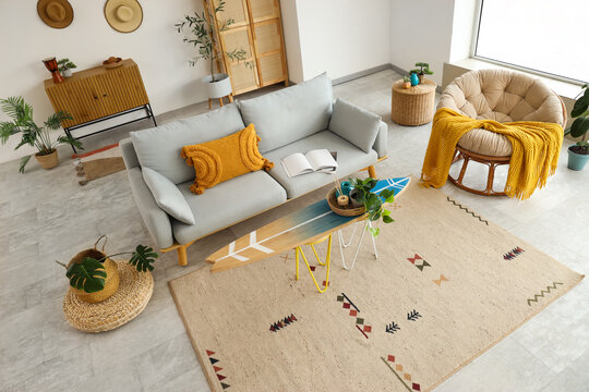 Fototapeta Interior of living room with surfboard, sofa and armchair