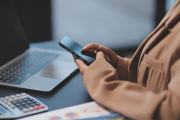 Young beautiful Asian businesswoman holding smartphone while working in the office room.