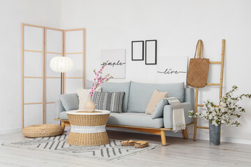 Interior of light living room with sofa, folding screen and flowering branches in vases