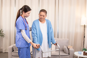 Fototapeta premium Young nurse assisting senior woman in walking with a walker, demonstrating caregiving, encouragement, and physical rehabilitation at home, healthcare, caregiver, medical, hospitality, recover.